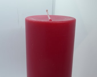 May include: A solid red pillar candle with a white wick. The candle is cylindrical and stands upright against a white background. The candle is a deep, rich red color.