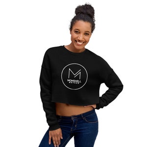 Peut inclure: Sweat-shirt noir court avec un logo circulaire blanc qui dit "Momshell Method" et un "M" stylisé à l'intérieur du cercle.