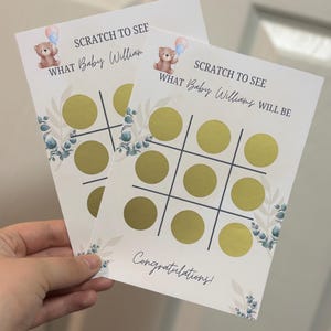 May include: Two baby shower scratch-off cards with a tic-tac-toe grid and gold scratch-off circles. The cards feature a teddy bear with balloons and the text "SCRATCH TO SEE WHAT Baby Willian/Williams WILL BE". The cards also say "Congratulations!"