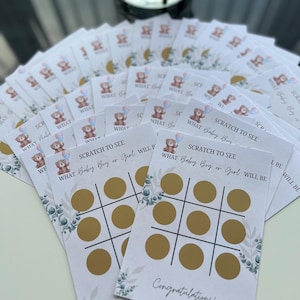 May include: A stack of baby shower scratch-off game cards. Each card features a tic-tac-toe grid with gold circles, the text "SCRATCH TO SEE WHAT Baby Boy or Girl WILL BE", and a teddy bear graphic. The word "Congratulations!" is printed at the bottom.