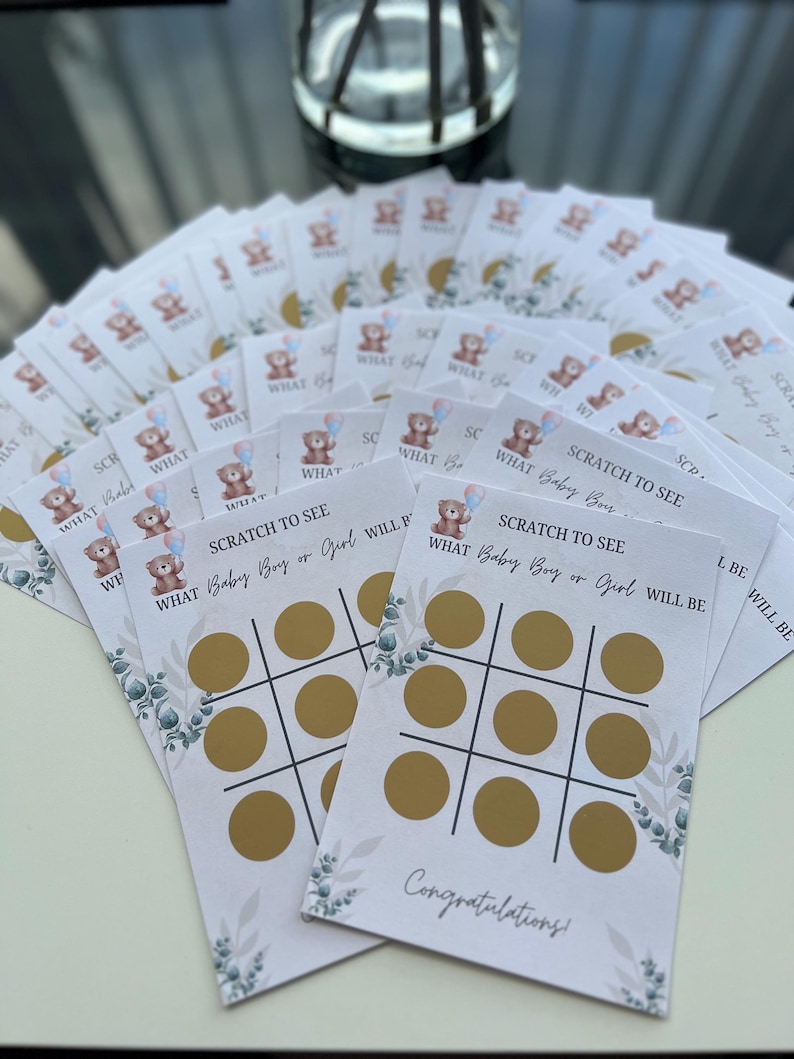 May include: A stack of baby shower scratch-off game cards. Each card features a tic-tac-toe grid with gold circles, the text "SCRATCH TO SEE WHAT Baby Boy or Girl WILL BE", and a teddy bear graphic. The word "Congratulations!" is printed at the bottom.