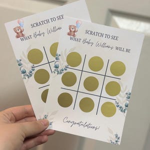 May include: Two baby shower scratch-off cards with a tic-tac-toe grid and gold circles. The cards feature a teddy bear with balloons, floral accents, and the text "SCRATCH TO SEE WHAT Baby William/Williams WILL BE" and "Congratulations!".