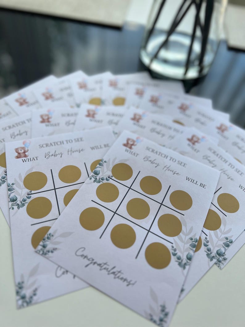 May include: A stack of baby shower scratch-off game cards. Each card features a tic-tac-toe grid with gold circles, the text "SCRATCH TO SEE WHAT Baby House WILL BE," and a "Congratulations!" message. Decorative floral elements are also present.