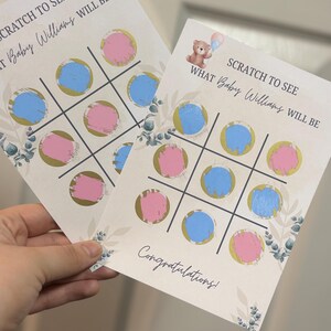 May include: Two gender reveal scratch-off cards with a tic-tac-toe design. Each card features blue and pink circles, gold accents, and the text "SCRATCH TO SEE WHAT Baby Williams WILL BE". A teddy bear graphic is also present.
