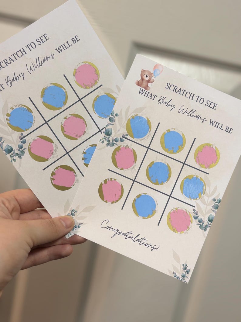 May include: Two gender reveal scratch-off cards with a tic-tac-toe design. Each card features blue and pink circles, gold accents, and the text "SCRATCH TO SEE WHAT Baby Williams WILL BE". A teddy bear graphic is also present.