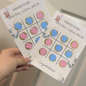 May include: Two baby shower scratch-off cards with a tic-tac-toe design. The cards have blue and pink circles, with text that reads "SCRATCH TO SEE WHAT Baby Williams WILL BE." A teddy bear graphic is at the top.