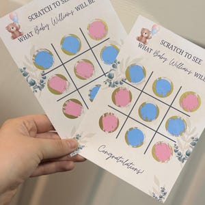 May include: Two baby shower scratch-off cards with a tic-tac-toe grid featuring pink and blue circles. The cards have text that reads "SCRATCH TO SEE WHAT Baby Williams WILL BE" and "Congratulations!" A teddy bear graphic is also present.