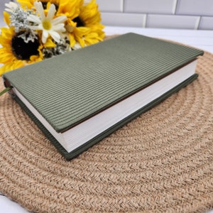 May include: A green journal with a textured fabric cover. The journal is closed and lying on a woven surface.