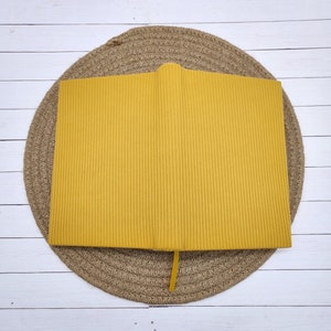 May include: A yellow ribbed notebook with a yellow ribbon bookmark. The notebook is sitting on a woven straw mat.