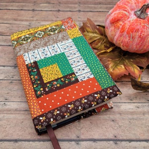 Può includere: Una copertina per libro rettangolare caratterizzata da un design patchwork realizzato con vari tessuti di cotone nei toni dell'arancione, giallo, verde, marrone e bianco. I motivi includono stampe floreali, pois e disegni geometrici.