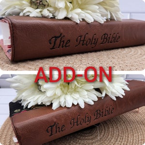 以下が含まれることがあります： 表紙に「The Holy Bible」という文字が刻まれた茶色の革装丁の聖書。白い花で飾られています。