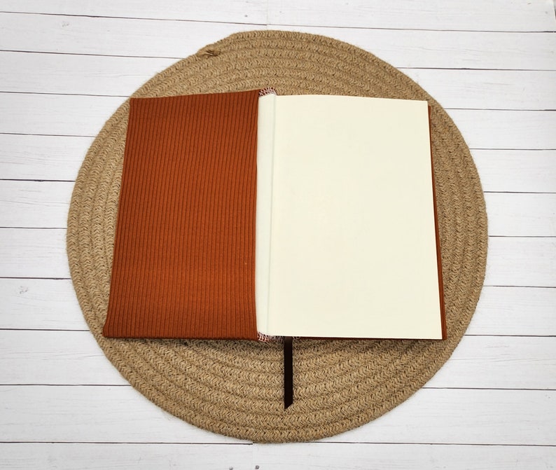 May include: A brown ribbed notebook with a blank white page open. The notebook is lying on a woven straw mat.