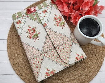 May include: A rectangular fabric book cover featuring a patchwork design of various floral patterns in shades of red, green, and cream. The cover displays diamond and triangular segments joined by visible stitching, with a dark ribbon bookmark.