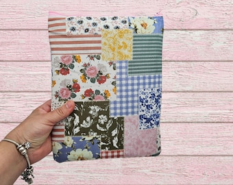 May include: A patchwork fabric pouch with a pink zipper. The pouch is made of various fabric squares with floral, striped, and gingham patterns in shades of pink, blue, green, and yellow. The pouch is held in a hand.
