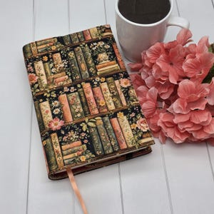 May include: A rectangular book cover featuring a black background with a repeating pattern of vintage-style books arranged on shelves, interspersed with small yellow and pink floral illustrations, accompanied by a light pink ribbon bookmark.