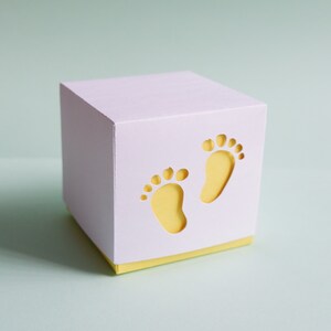 May include: A white gift box with a yellow lid. The box has two cut-out footprints on the front.