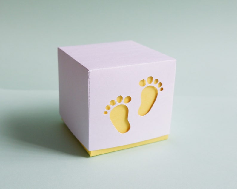 May include: A white gift box with a yellow lid. The box has two cut-out footprints on the front.