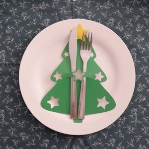 May include: A white plate with a green paper Christmas tree cutout holding a silver fork and knife. The tree has a yellow star on top.