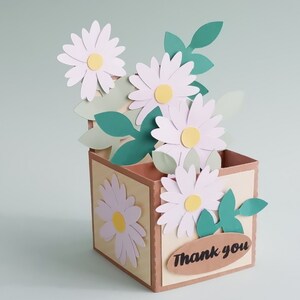 May include: A brown paper box with a "Thank You" label and a bouquet of white paper daisies with green paper leaves.