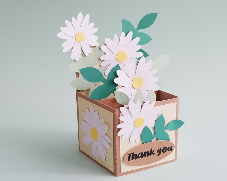 May include: A brown paper box with a "Thank You" label and a bouquet of white paper daisies with green paper leaves.