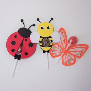May include: Three lollipop craft kits featuring a ladybug, a bee, and a butterfly. Each kit includes a pre-cut design, a lollipop, and a stick.