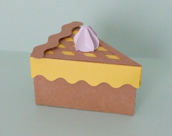 May include: A brown cardboard pie box with a yellow crust and a purple whipped cream topping. The box is shaped like a slice of pie.