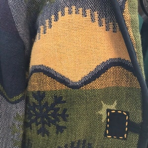 May include: A blue, green, and yellow woven jacket with a snowflake and star design. The jacket has a black trim and a patch on the sleeve.