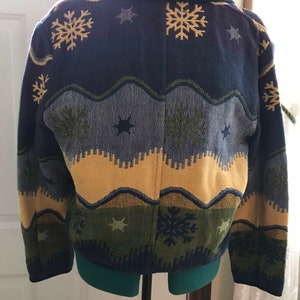 May include: A blue, green, yellow, and gray patterned cardigan with a snowflake and star design.