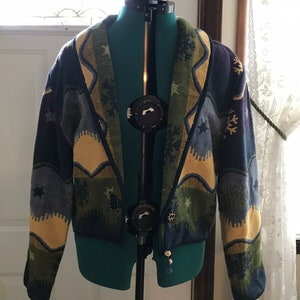May include: A blue, green, and yellow patterned cardigan with a shawl collar. The cardigan has a snowflake and star design.