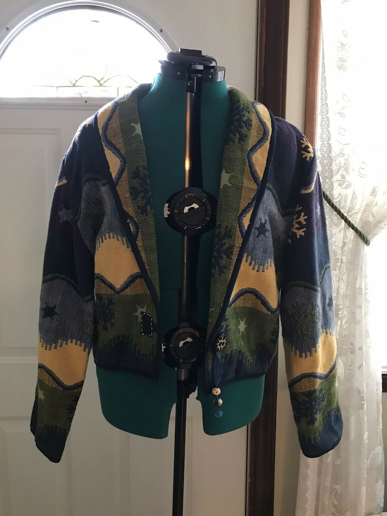 May include: A blue, green, and yellow patterned cardigan with a shawl collar. The cardigan has a snowflake and star design.