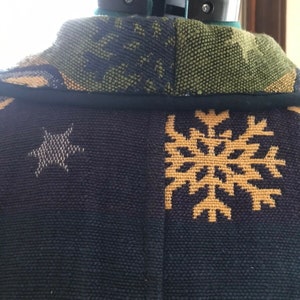 May include: Black and green patterned fabric with a gold snowflake and star design. The fabric is woven with a textured surface.