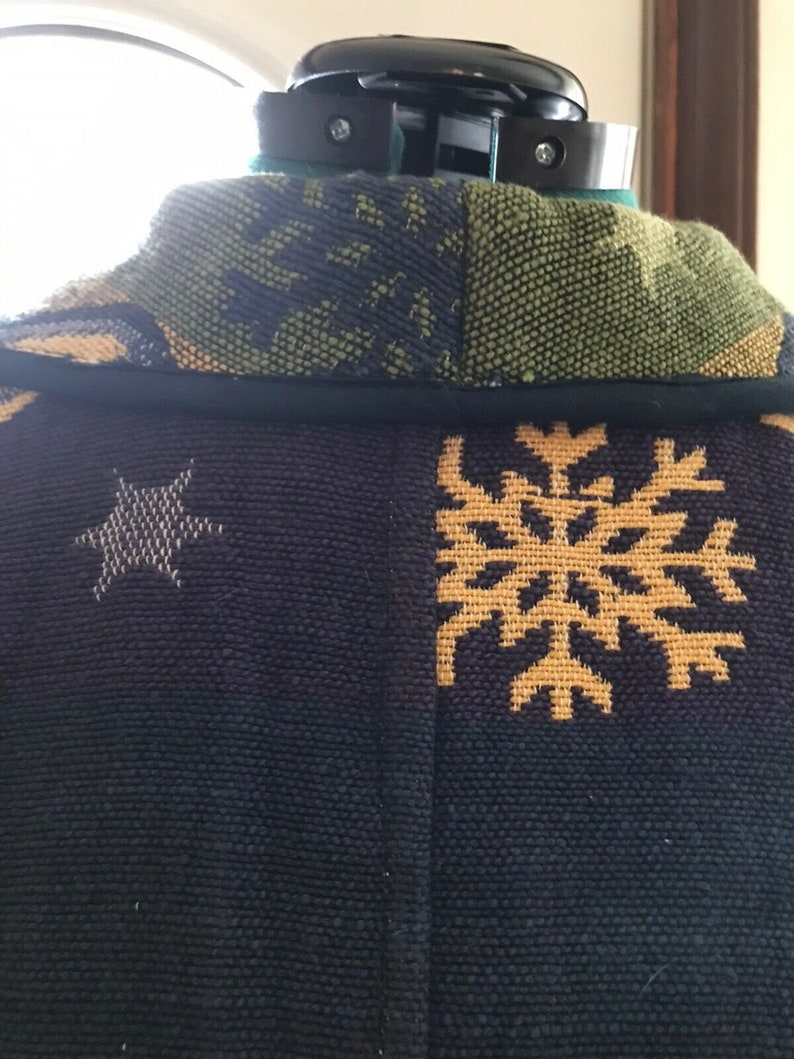 May include: Black and green patterned fabric with a gold snowflake and star design. The fabric is woven with a textured surface.