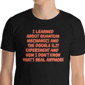 以下が含まれることがあります： オレンジ色の文字「I LEARNED ABOUT QUANTUM MECHANICS AND THE DOUBLE SLIT EXPERIMENT AND NOW I DON'T KNOW WHAT'S REAL ANYMORE」が書かれた黒いTシャツ。