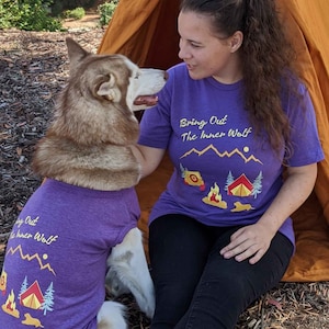 Woman and her large dog wearing matching dog and owner camping shirts in purple that say Bring Out the Inner Wolf