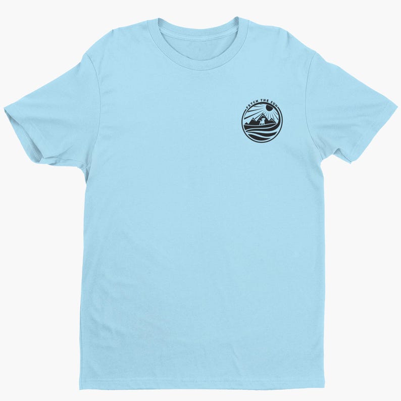 May include: A light blue short-sleeve t-shirt featuring a circular black graphic on the upper left chest. The graphic depicts a mountain landscape with a sun and a dog, surrounded by the text "FETCH THE SUN" in a circular border.