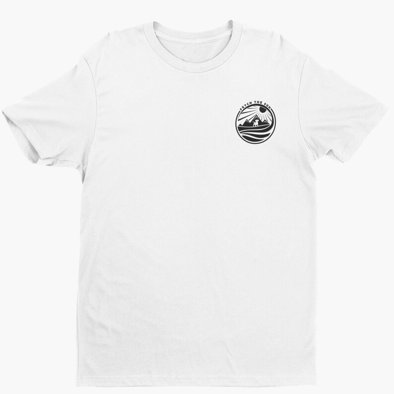 May include: A white short-sleeved t-shirt featuring a small circular black graphic on the upper left chest. The graphic depicts a dog standing on a hill with mountains and a sun in the background, surrounded by the text FETCH THE SUN.