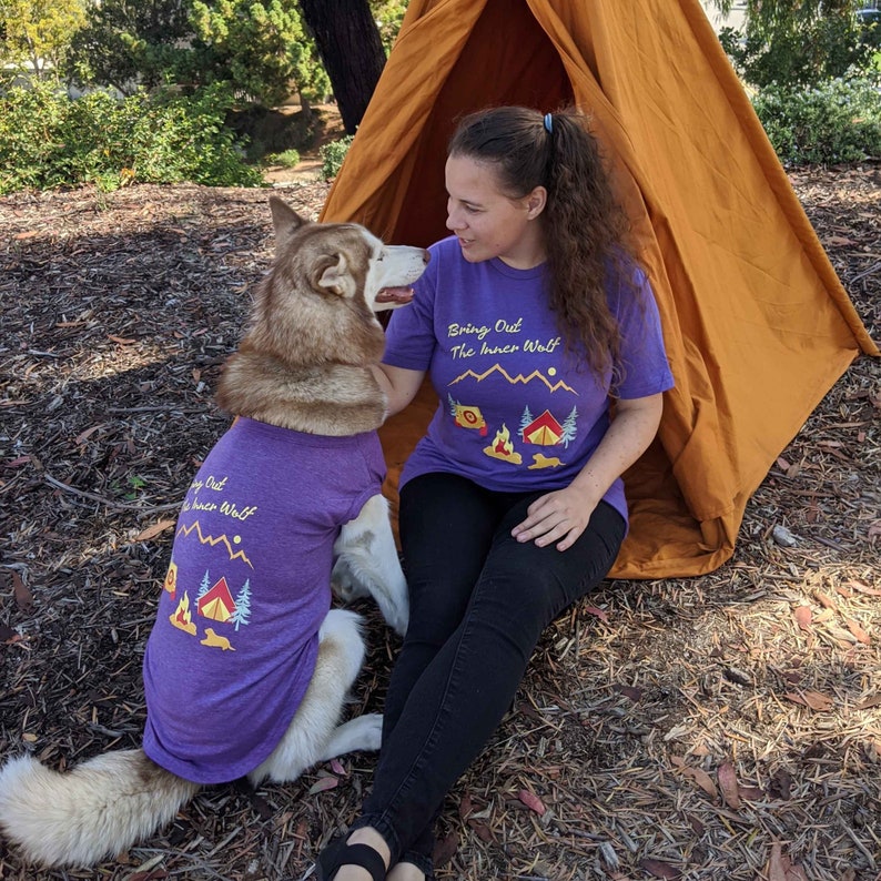 Woman and her large dog wearing matching dog and owner camping shirts in purple that say Bring Out the Inner Wolf