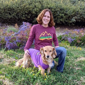 Woman and her dog on a trail wearing matching hiking shirts that say Get Your Tails on the Trails.