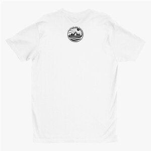 May include: A plain white short-sleeved t-shirt featuring a circular black graphic on the upper back. The design depicts a dog silhouette standing before mountains and a sun, with the text FETCH THE SUN arched along the top of the circle.