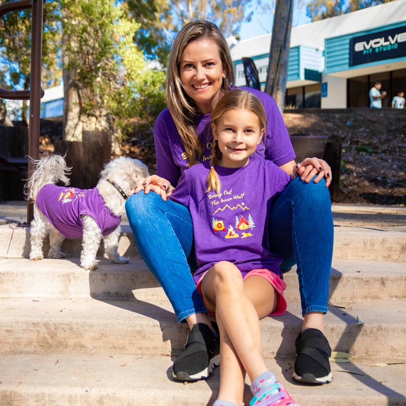 Mom, daughter, and dog all wearing matching dog and owner camping shirts in purple that say Bring Out the Inner Wolf