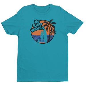 May include: A teal short-sleeved t-shirt featuring a circular graphic on the chest. The design displays an orange sunset, a blue ocean, palm trees, a silhouette of a person with a surfboard, and a dog, with the text NO RUFF WAVES in blue.