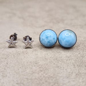 Può includere: Un paio di orecchini d'argento con una pietra preziosa blu e un design a stella marina.
