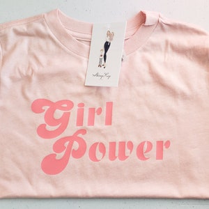 May include: A pink t-shirt with the words "Girl Power" printed in a pink retro font.