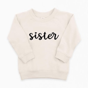 May include: A cream colored sweatshirt with a black cursive word "sister" with a small heart above the "s".