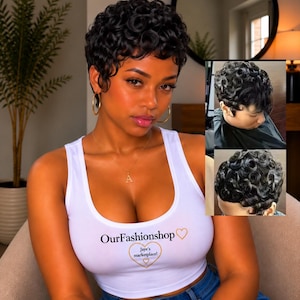 May include: A white sleeveless tank top featuring the text OurFashionshop with a heart icon and a smaller heart containing the text Jaye's marketplace!. The top is worn with blue denim jeans and gold hoop earrings, paired with a short curly hairstyle.