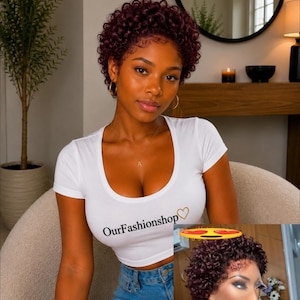 May include: A short, curly, deep burgundy wig with a natural-looking lace front hairline. The hair is styled in tight, voluminous ringlets that frame the face. The wig features a dark root transition and a realistic scalp appearance at the part.