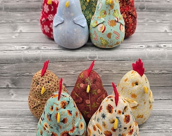 May include: A collection of ten fabric chicken figurines featuring various patterns including floral, holiday, and solid colors. Each chicken has a red felt comb, a yellow beak, and a rounded body shape, arranged in two rows on a gray wood surface.