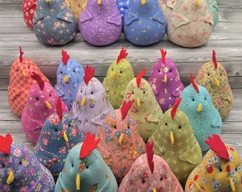 May include: A collection of twenty-five plush fabric chickens in various colors and floral patterns. Each stuffed chicken features a bright red felt comb, a small yellow felt beak, and two black bead eyes, arranged in rows.