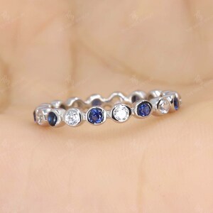 Puede incluir: Una banda de eternidad delicada con zafiros azules y diamantes blancos alternos engastados en una banda plateada.