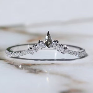 May include: A delicate silver ring with a small, pointed diamond in the center and smaller diamonds lining the band. The ring is curved in a crescent shape.